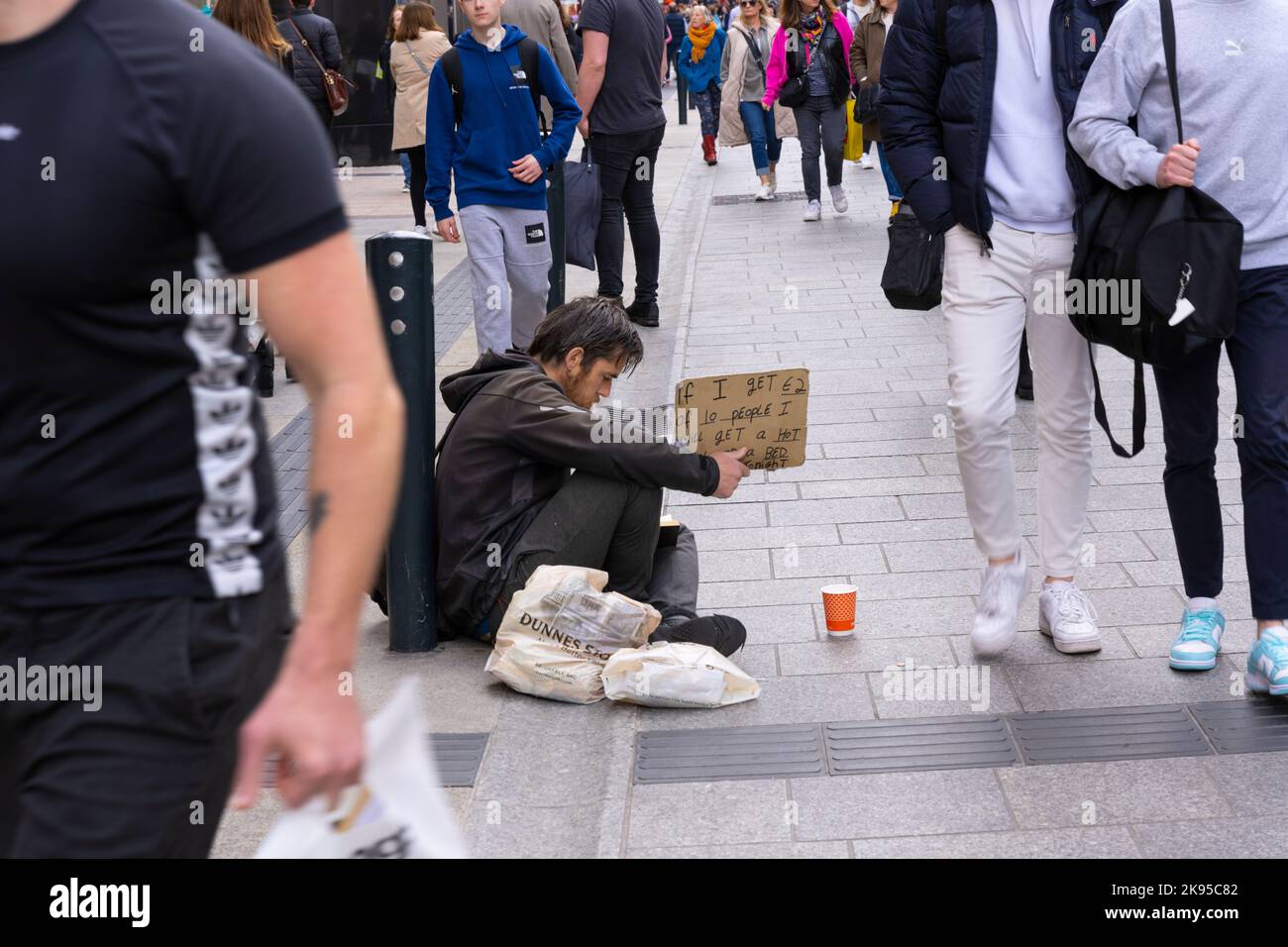Irlanda Dublino Grafton Street Beggar mendicante giovane uomo senza casa segno - se ho €2 euro da 10 persone mi verrà un pasto caldo e un letto Tonight Foto Stock