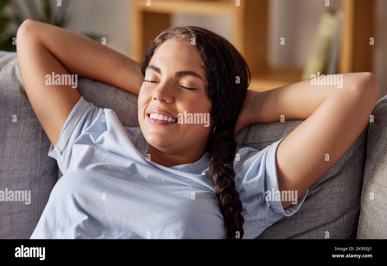 Donna, sorridere e rilassarsi sul divano in soggiorno con felice in vacanza, vacanza o pausa in casa. Felicità, casa e divano con donna in libertà, sé Foto Stock