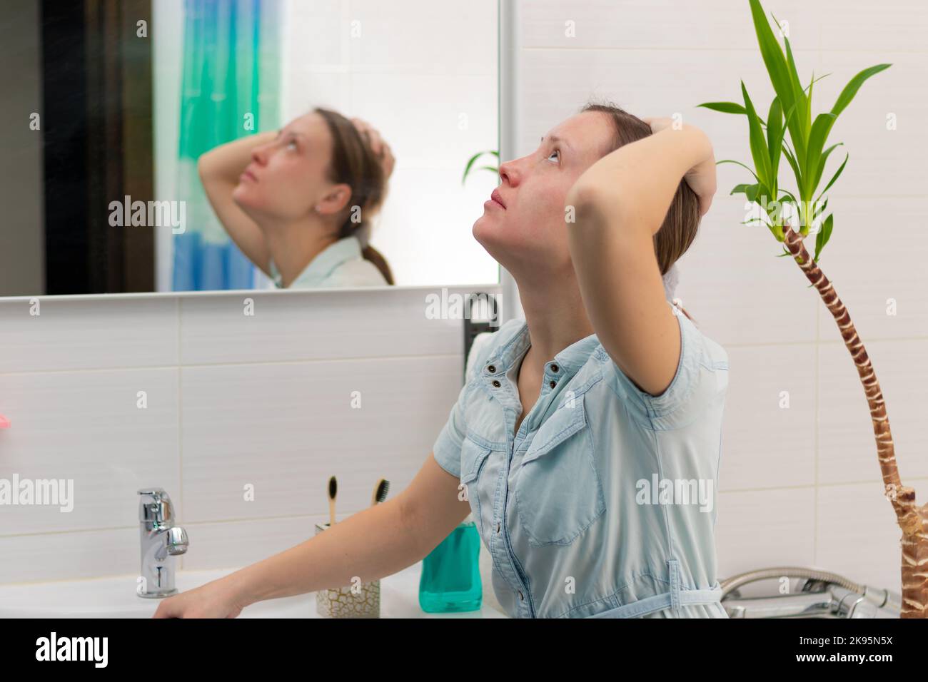 Una giovane donna pulitore in un bagno luminoso con uno stantuffo per eliminare il blocco nelle sue mani. Sul muro c'è uno specchio con un riflesso. Pianta verde. Foto Stock