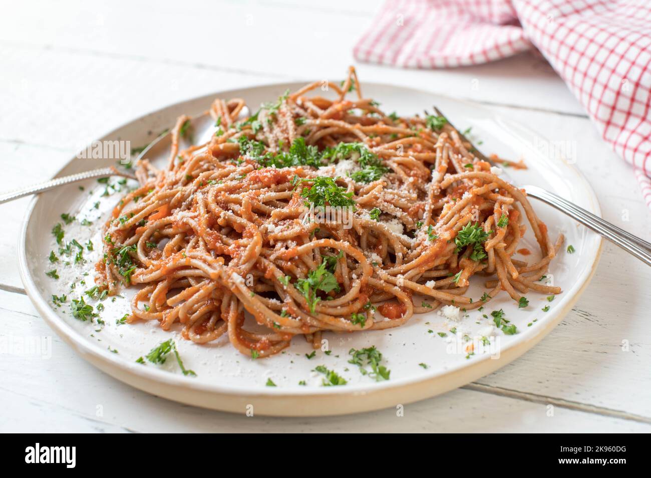 Spaghetti di grano intero con salsa di pomodoro fatta in casa e parmigiano su un piatto isolato su fondo di legno bianco Foto Stock