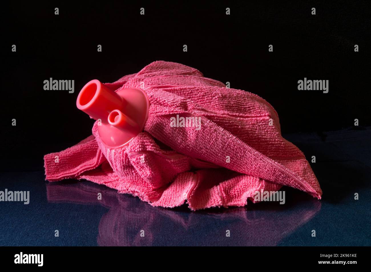 Una testina in microfibra rosa su un tavolo di vetro. Articoli per la casa con riflessi su sfondo nero Foto Stock