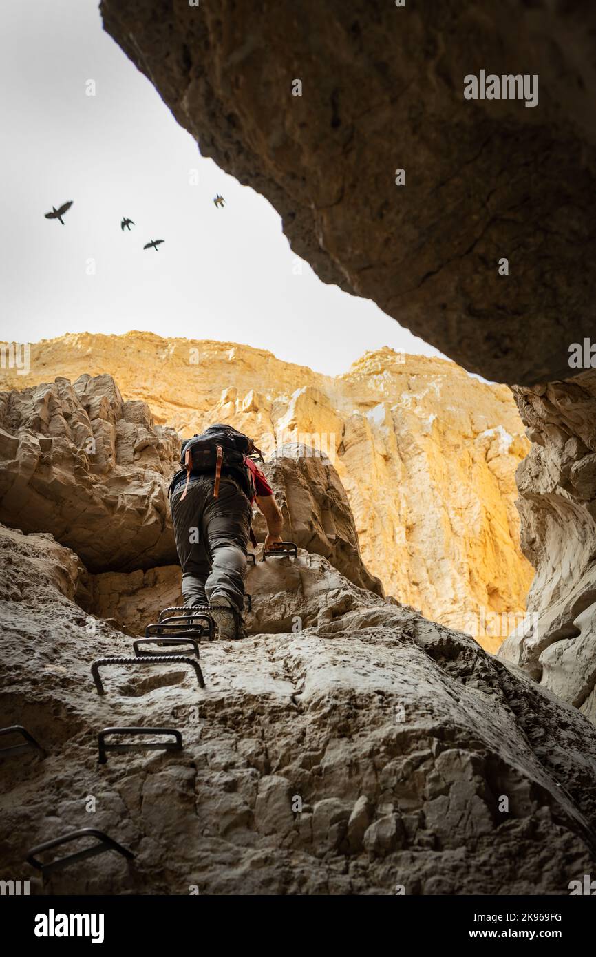 escursionista utilizzando pioli per salire su una roccia in un canyon del deserto Foto Stock