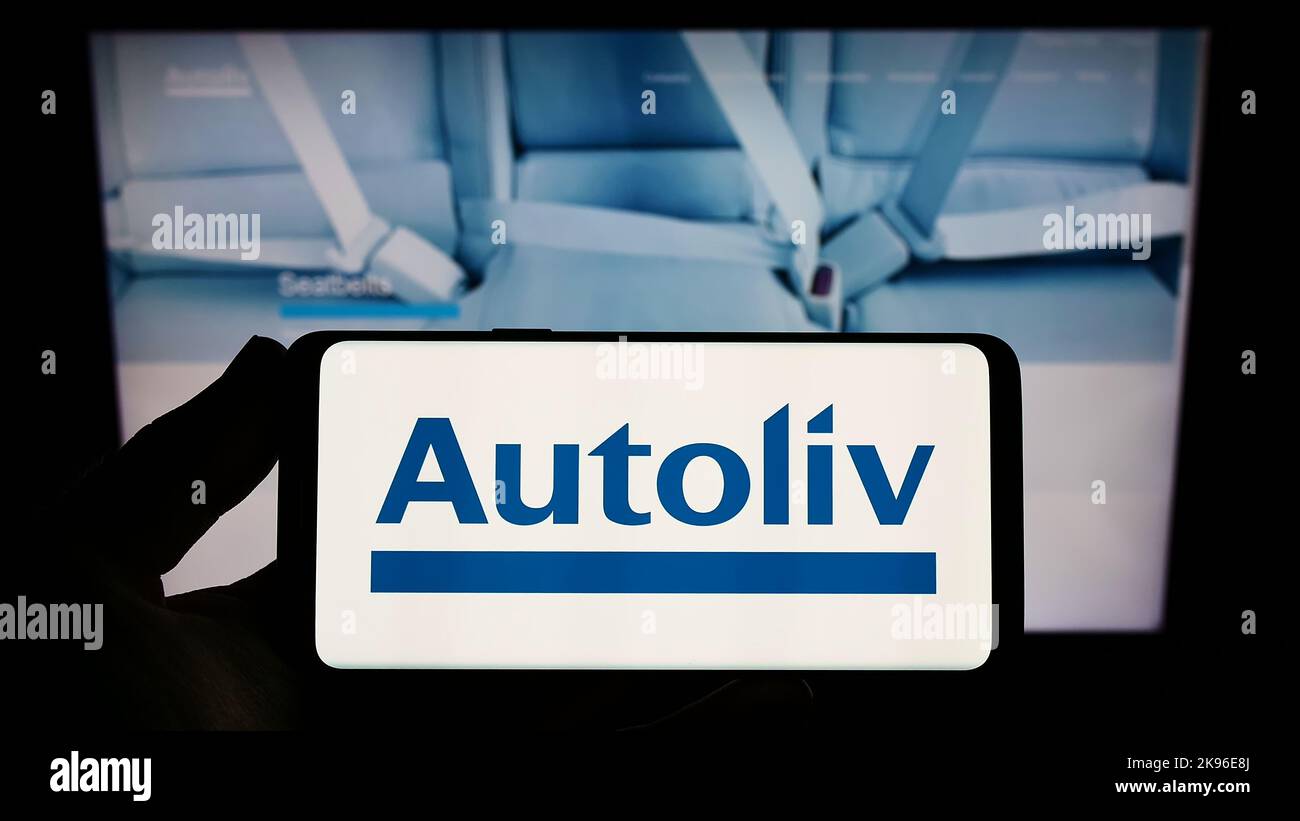 Persona in possesso di smartphone con il logo della società di fornitura automobilistica Autoliv Inc. Sullo schermo di fronte al sito Web. Messa a fuoco sul display del telefono. Foto Stock