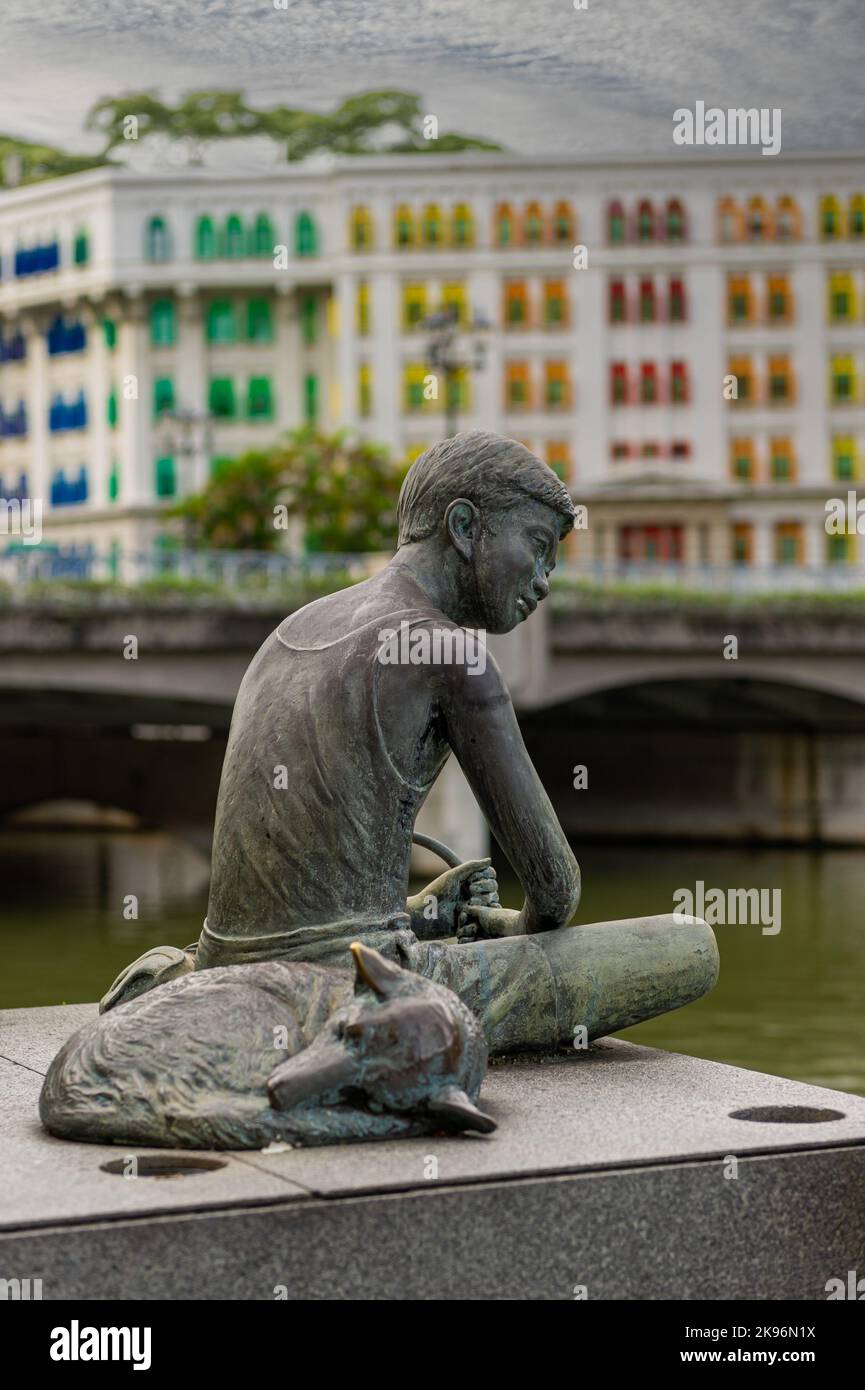 Ragazzo con il suo cane che pesca al fiume Singapore con la stazione di polizia di Old Hill Street sullo sfondo Foto Stock