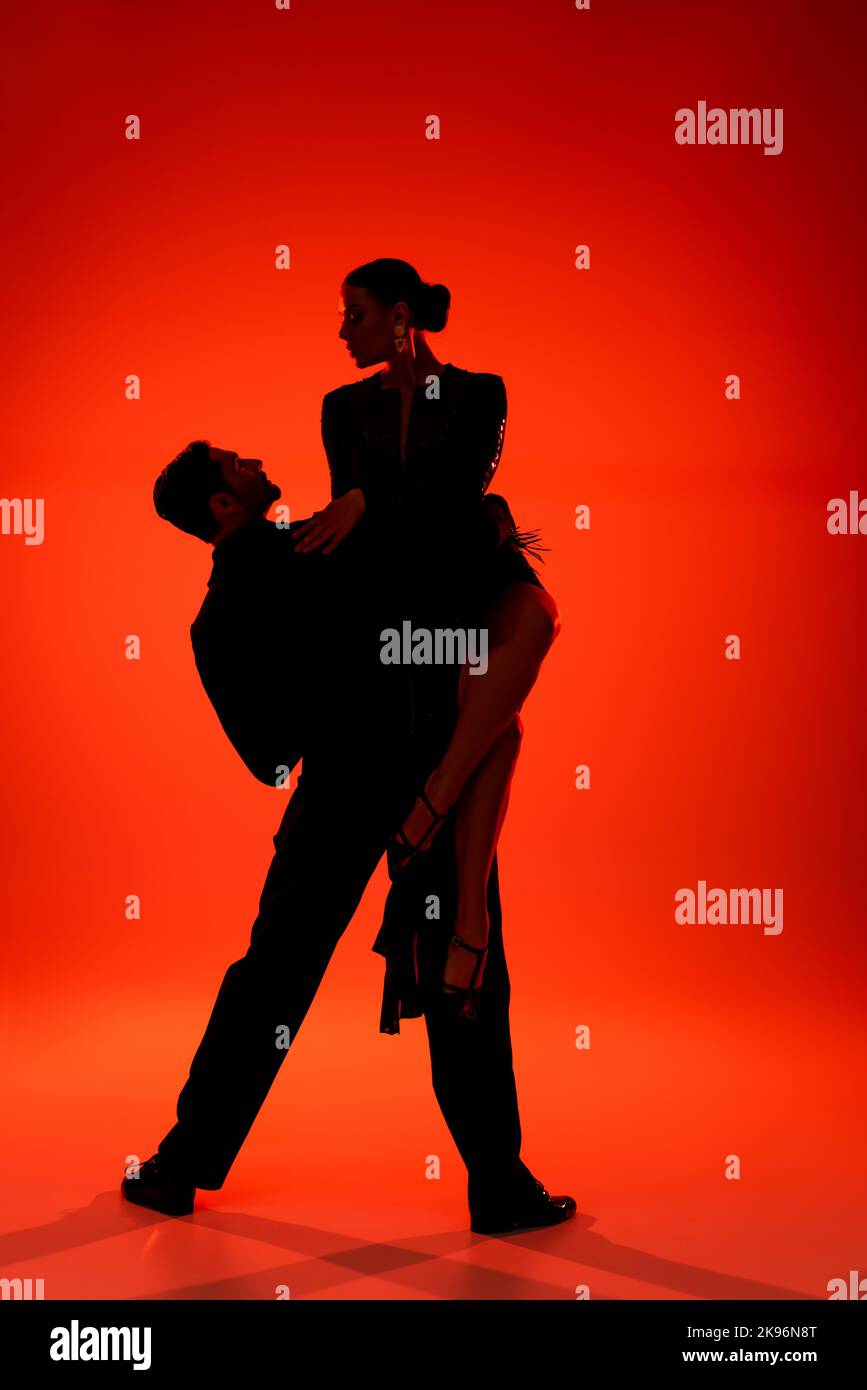 Silhouette di coppia di ballerini professionisti che eseguono tango su sfondo rosso Foto Stock