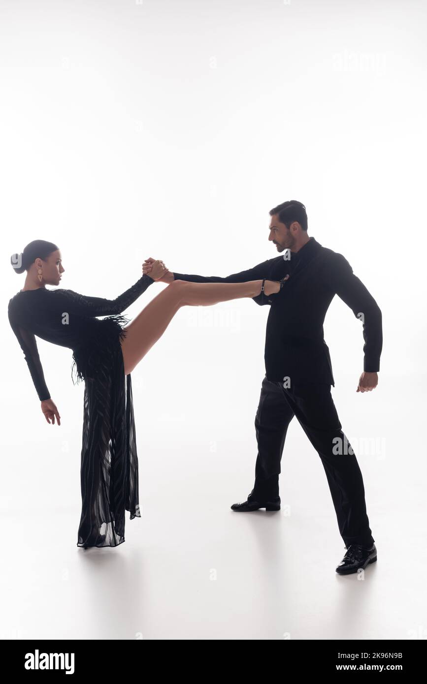 Vista laterale dei ballerini professionisti che tengono le mani mentre eseguono il tango su sfondo bianco Foto Stock