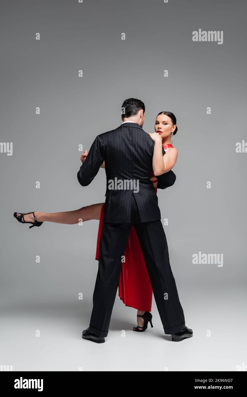 Donna elegante con tacchi che guarda la macchina fotografica mentre danzano il tango con il compagno su sfondo grigio Foto Stock