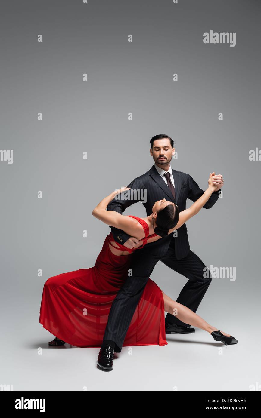 Ballerina in tuta che esegue tango con elegante partner su sfondo grigio Foto Stock