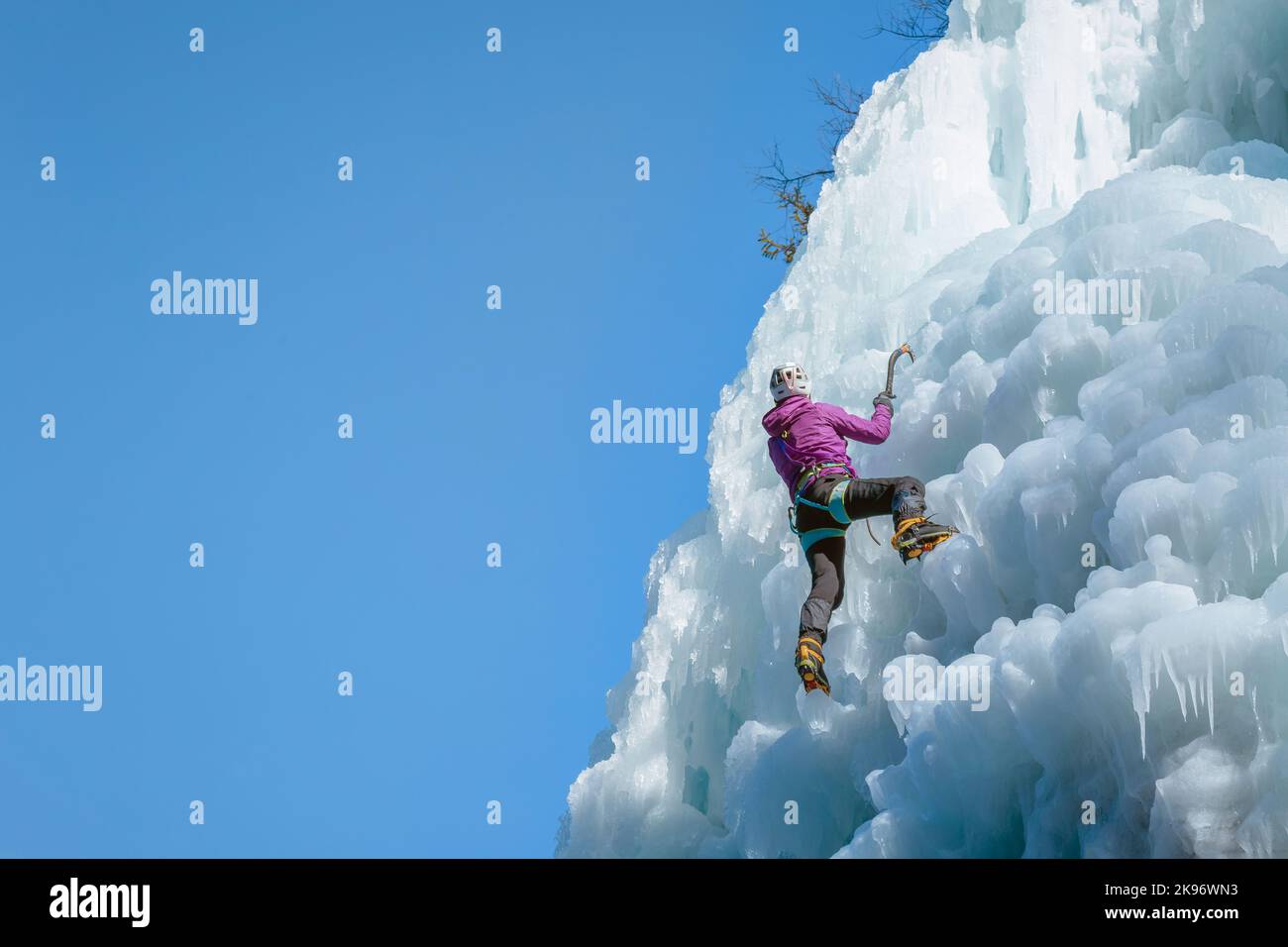 Donna alpinista con attrezzature per arrampicata su ghiaccio su una cascata ghiacciata Foto Stock