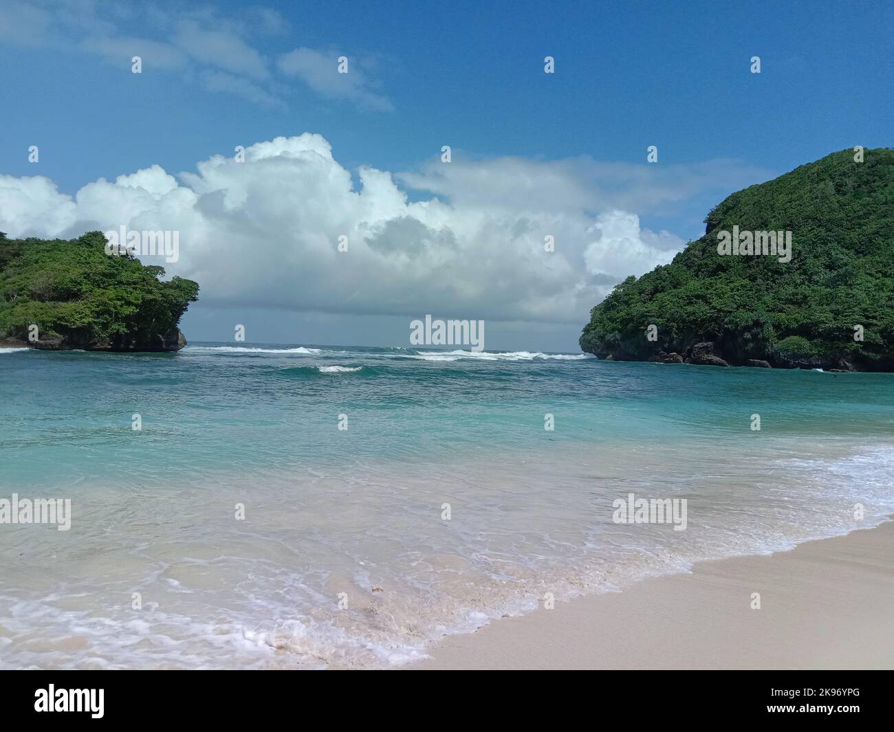 Una spiaggia di sabbia idilliaca con nuvole e scogliere boscose sullo sfondo in Indonesia Foto Stock