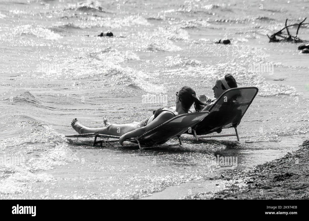 Due donne che si abbronzano su sedie a sdraio a South Lindstrom Lake presso il Beach Park a Lindstrom, Minnesota USA. Montaggio in bianco e nero. Foto Stock