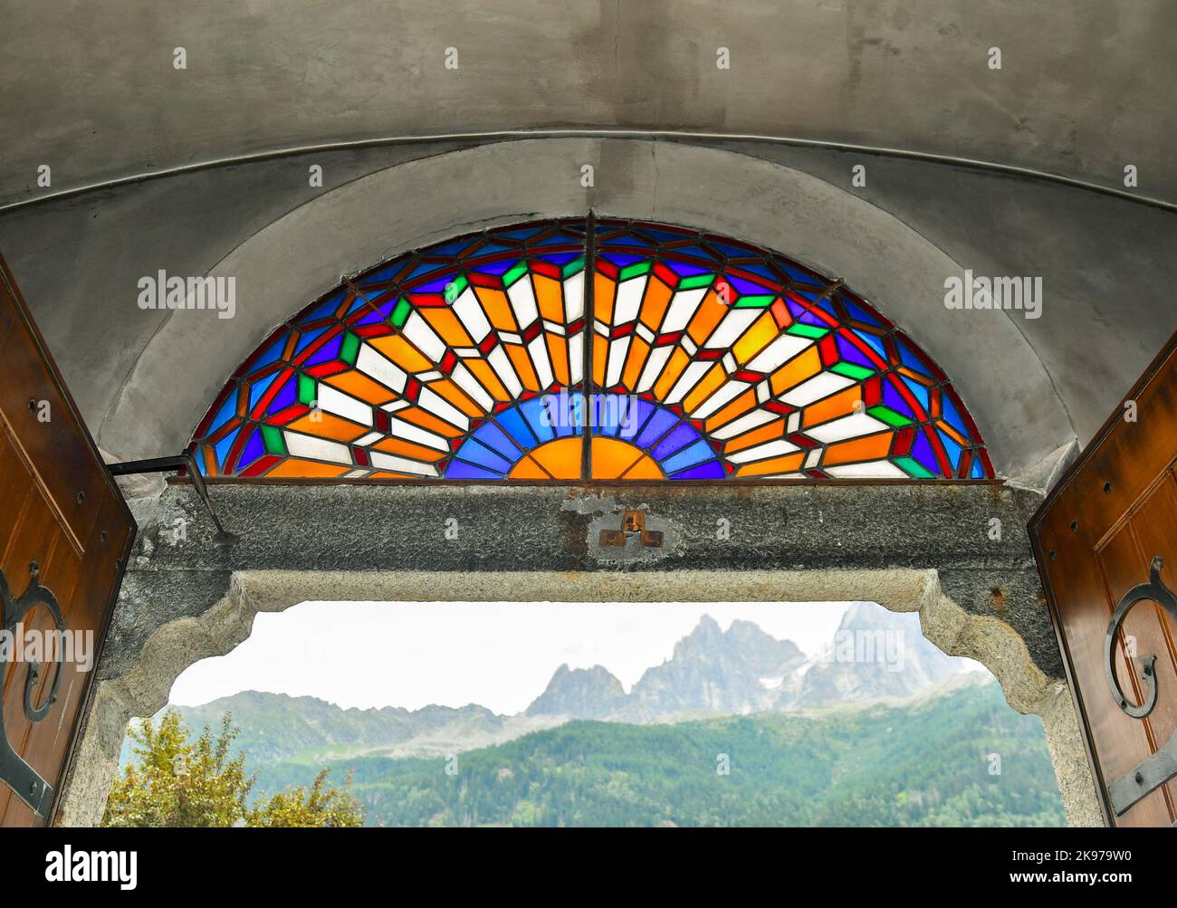 Vetrata colorata sopra la porta d'ingresso della Chiesa di Saint Michel con le vette delle Aiguilles sullo sfondo, Chamonix, Francia Foto Stock