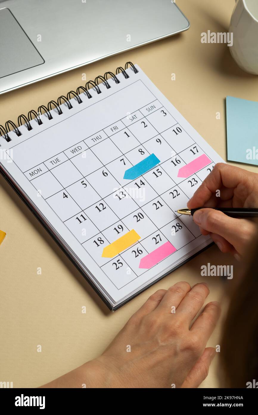 Mani di una donna che pianifica e che segna le date del calendario delle riunioni aziendali sul calendario. Foto Stock