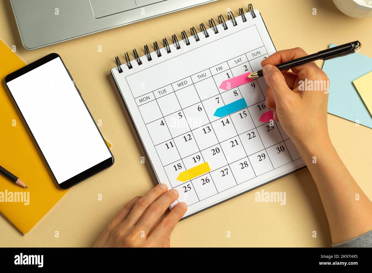 Telefono con schermo bianco e calendario con le date per la scrittura delle riunioni di lavoro. Concetto di pianificazione e scadenza. Una donna prende appunti per ricordare un Foto Stock