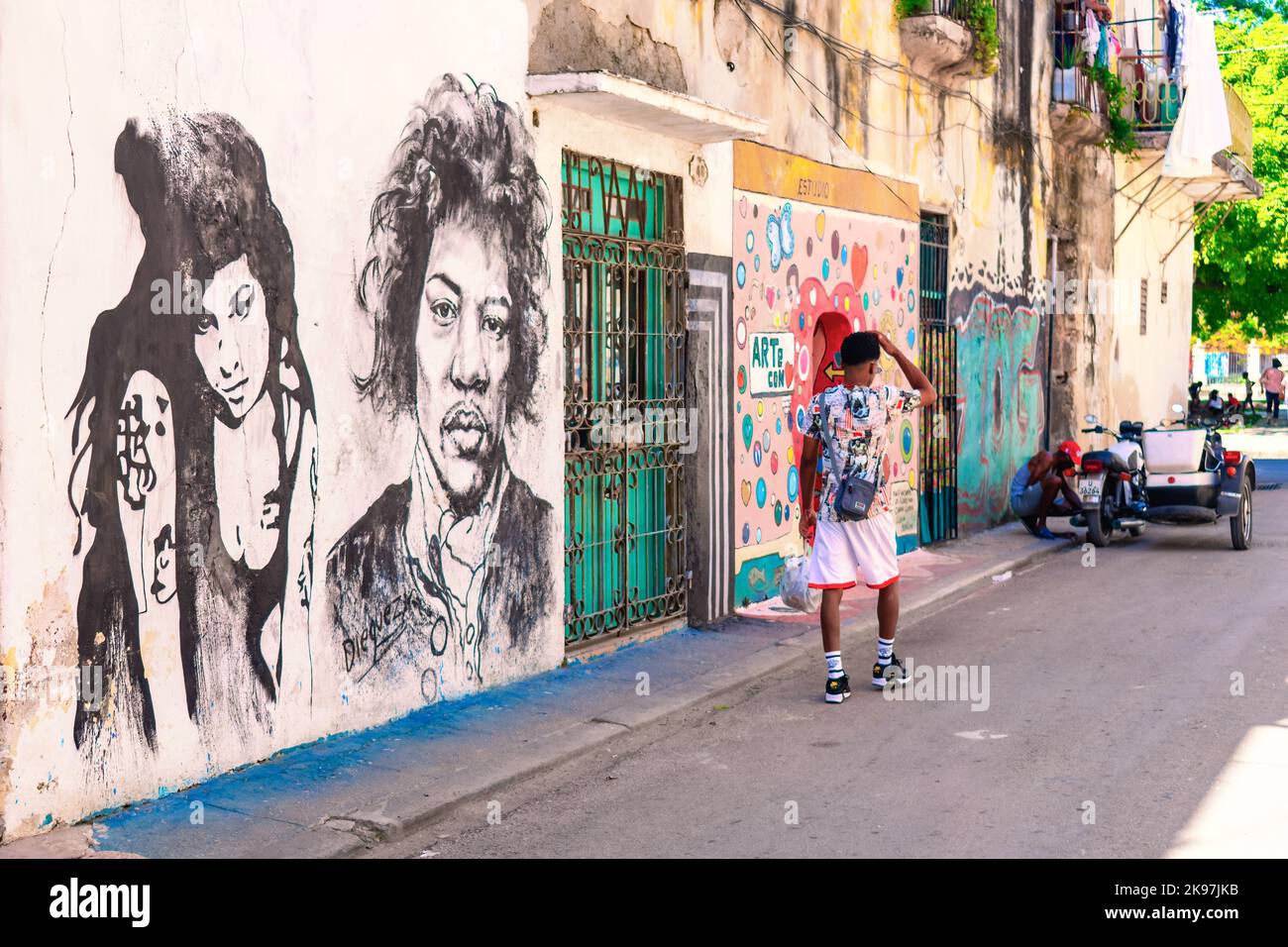 Un uomo a piedi da dipinti urbani o graffiti. L'edificio è protetto da una griglia metallica all'interno della porta. Foto Stock