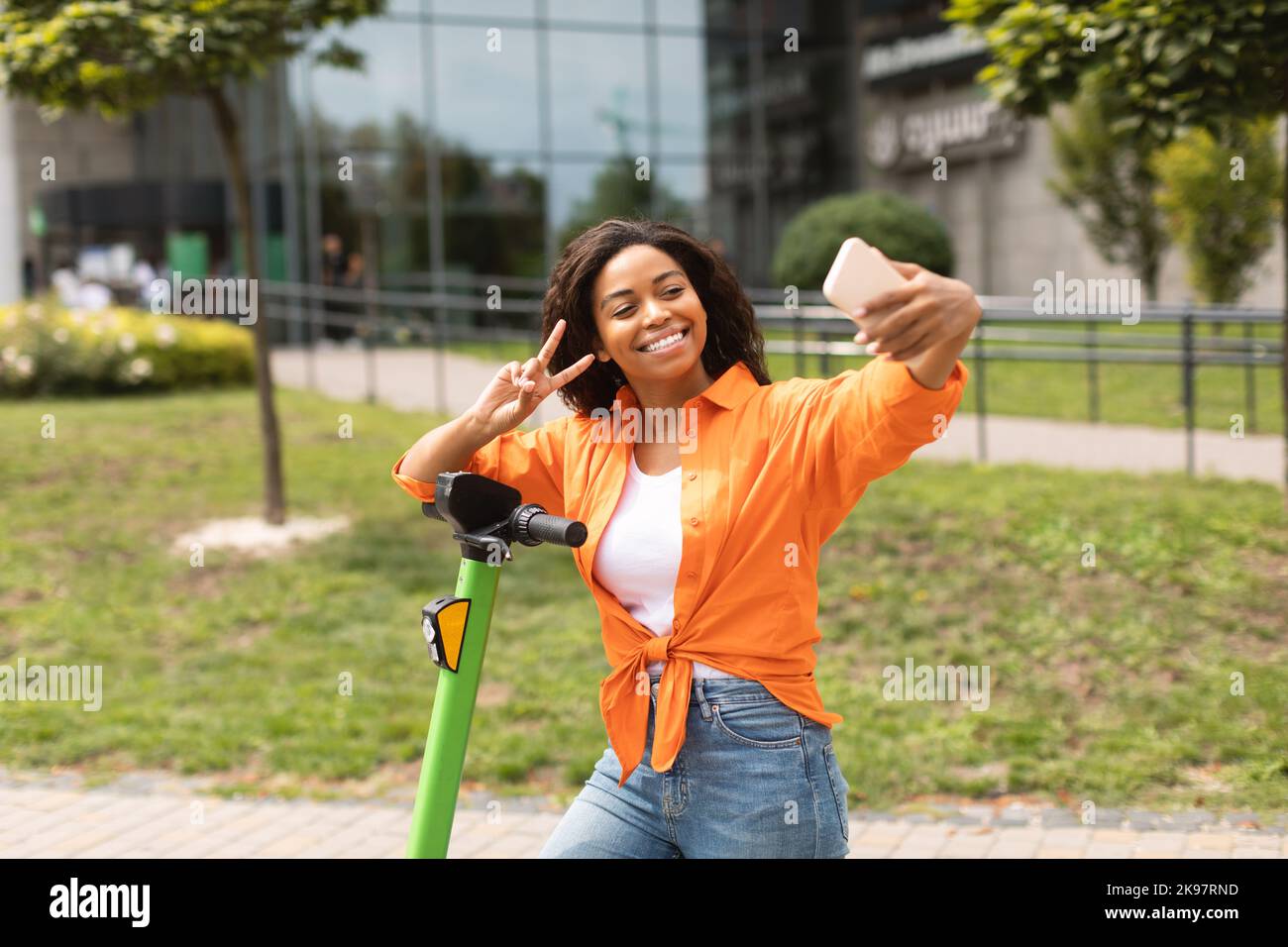 Sorridente ragazza afroamericana millenaria in casual prendere selfie su smartphone su scooter elettrico Foto Stock