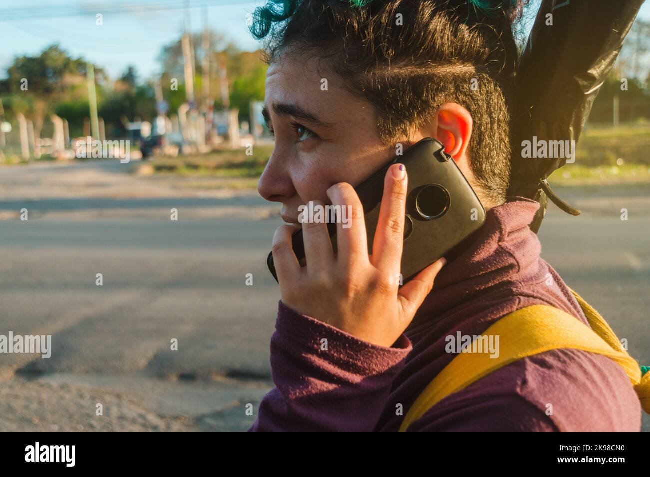 primo piano del profilo di una giovane donna viaggiatore caucasica latina, con capelli rasati, parlando al telefono all'aperto, camminando sul lato della strada Foto Stock