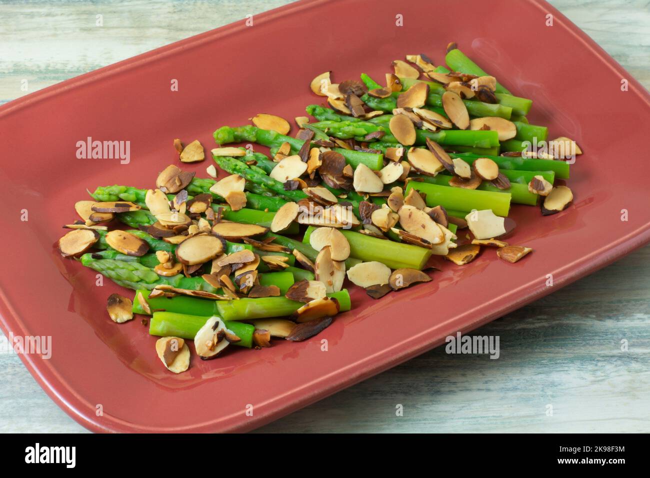 Contorno di asparagi e fette di mandorle tostate su piatto di portata rosso Foto Stock