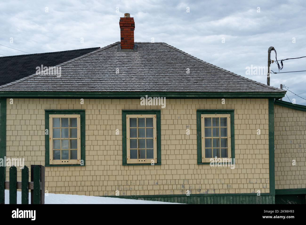 Una casa vintage in legno di cedro shake con tetto grigio hip in legno. L'edificio ha un camino di mattoni rossi e finestre multiple di vetro. Foto Stock