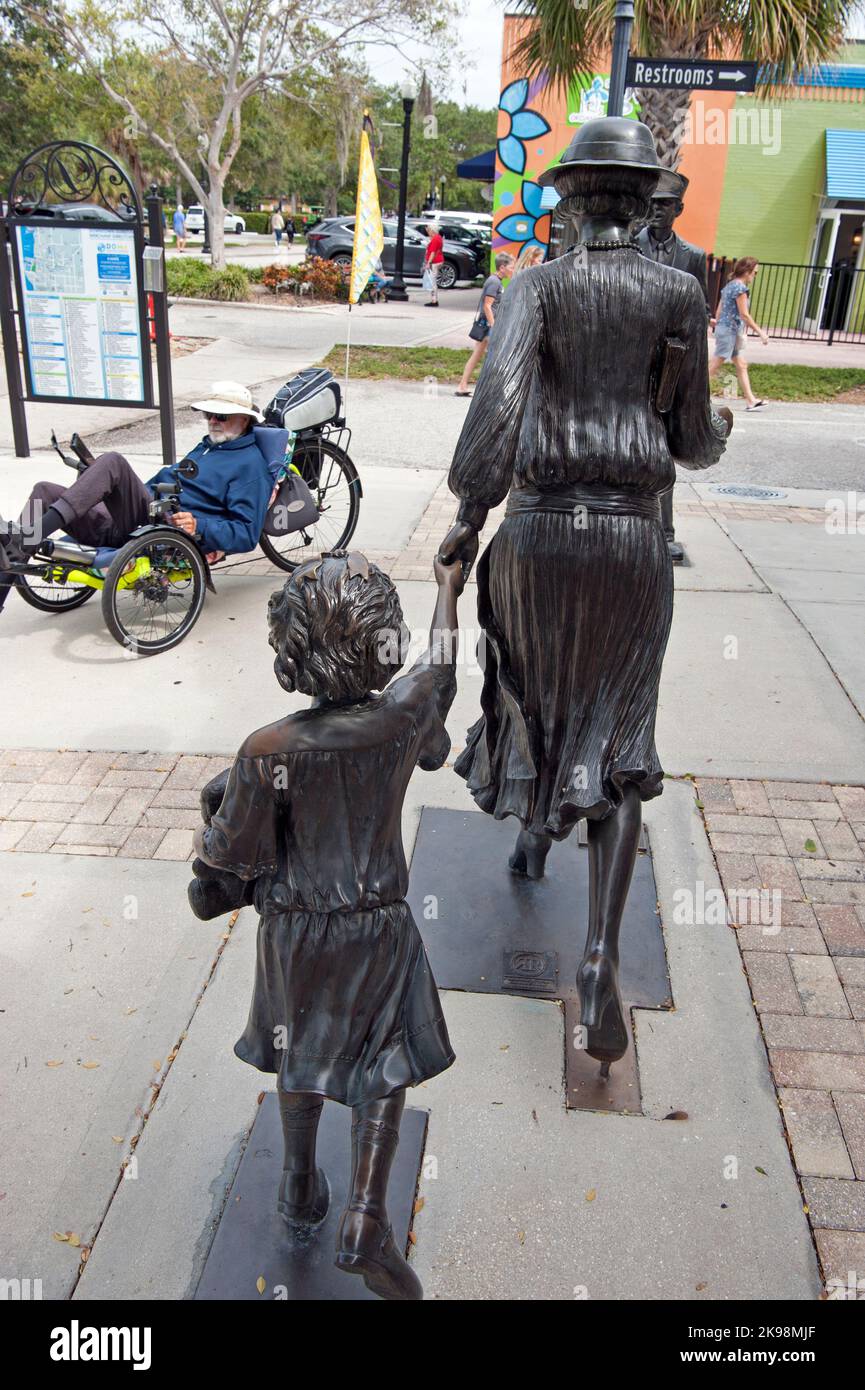 Un uomo anziano corre in bici a quattro ruote passando davanti a una scultura fuori dal Museo storico di Dunedin, Florida, USA. Foto Stock