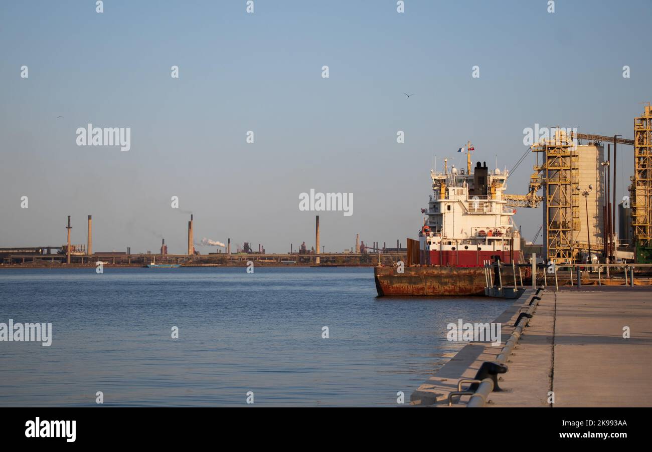 In una giornata limpida e soleggiata, una nave da carico rossa e bianca viene vista ormeggiata in un porto industriale nel tardo pomeriggio. Foto Stock