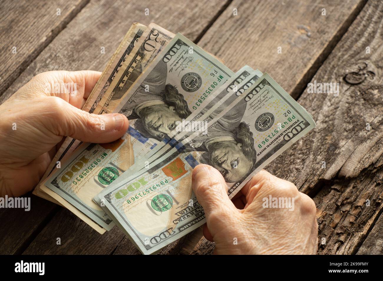 mani di una vecchia donna su dollari americani su un tavolo di legno primo piano Foto Stock