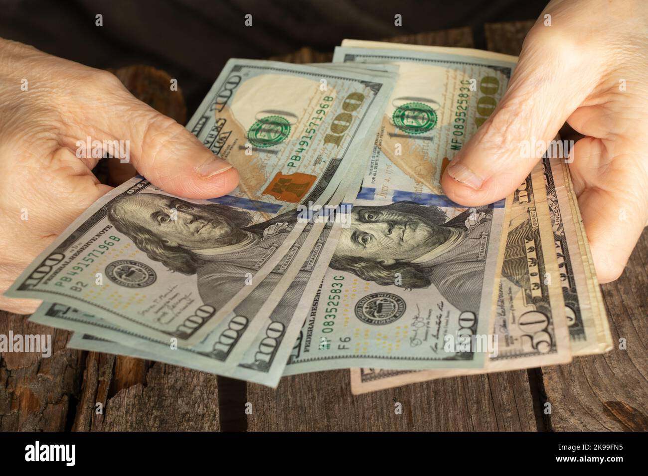 mani di una vecchia donna su dollari americani su un tavolo di legno primo piano Foto Stock