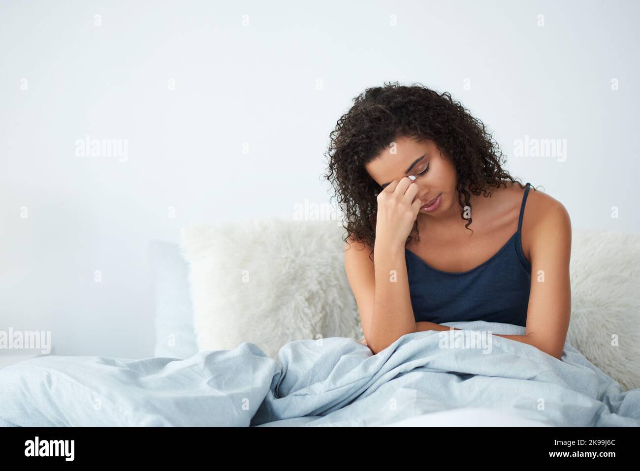 La mia testa fa male solo un po': Una giovane donna attraente che soffre di mal di testa e che si siede a letto pizzicando il naso al mattino. Foto Stock