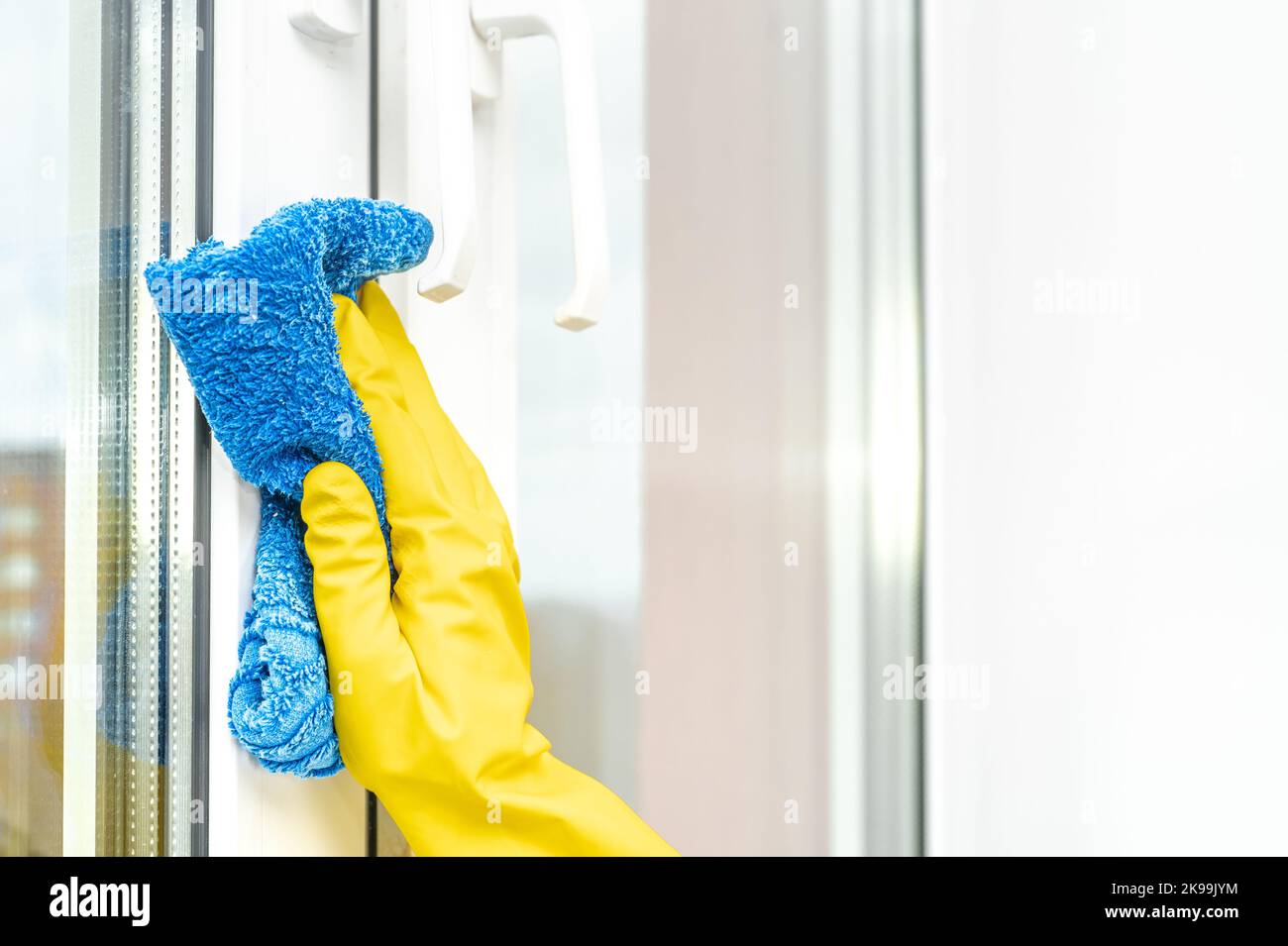 Servizio di pulizia. Mano femmina in guanto di gomma gialla con finestra di lavaggio in microfibra blu e telaio in plastica a casa, servizio di pulizia concetto Foto Stock