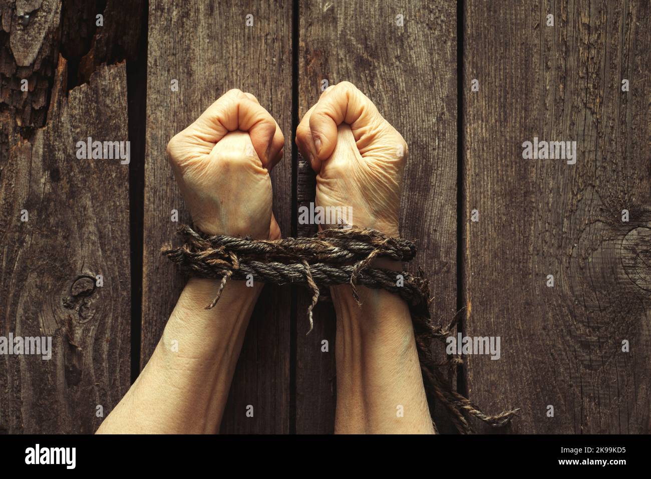 mani legate con corda di vecchia donna su tavola di legno Foto Stock