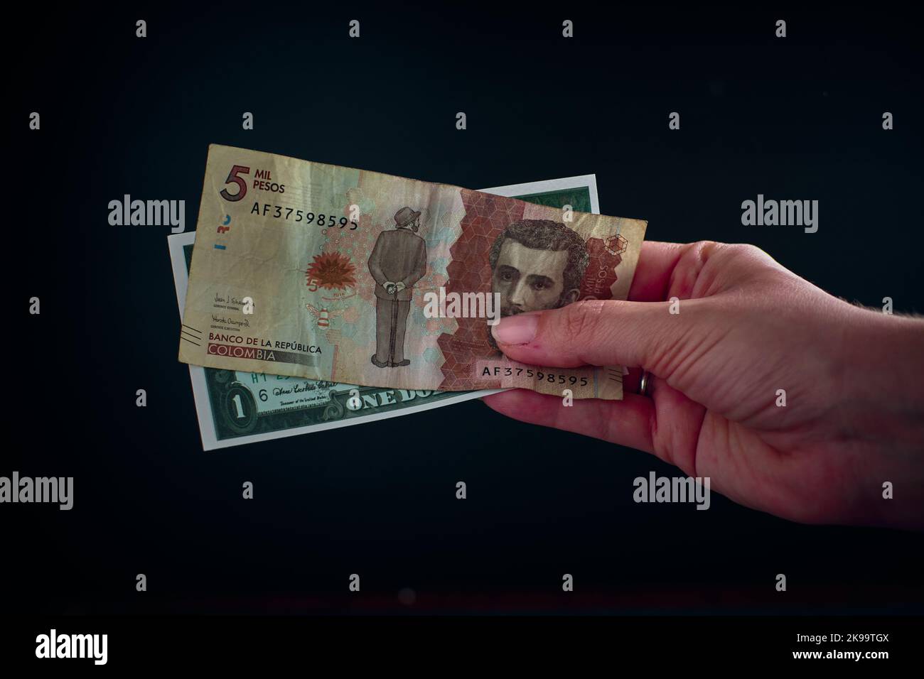 Una mano che tiene un disegno di legge di 5 mila pesos colombiani con 1 dollaro americano Foto Stock