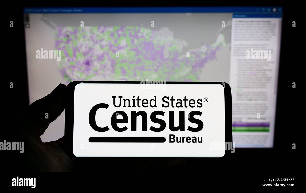 Persona che tiene uno smartphone con il logo dell'agenzia statunitense United States Census Bureau (USCB) sullo schermo di fronte al sito Web. Messa a fuoco sul display del telefono. Foto Stock