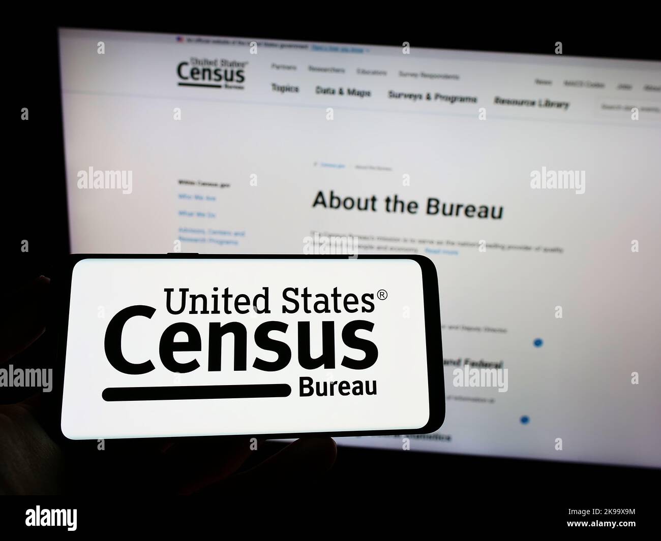 Persona che tiene il cellulare con il logo dell'agenzia statunitense United States Census Bureau (USCB) sullo schermo di fronte alla pagina web. Messa a fuoco sul display del telefono. Foto Stock