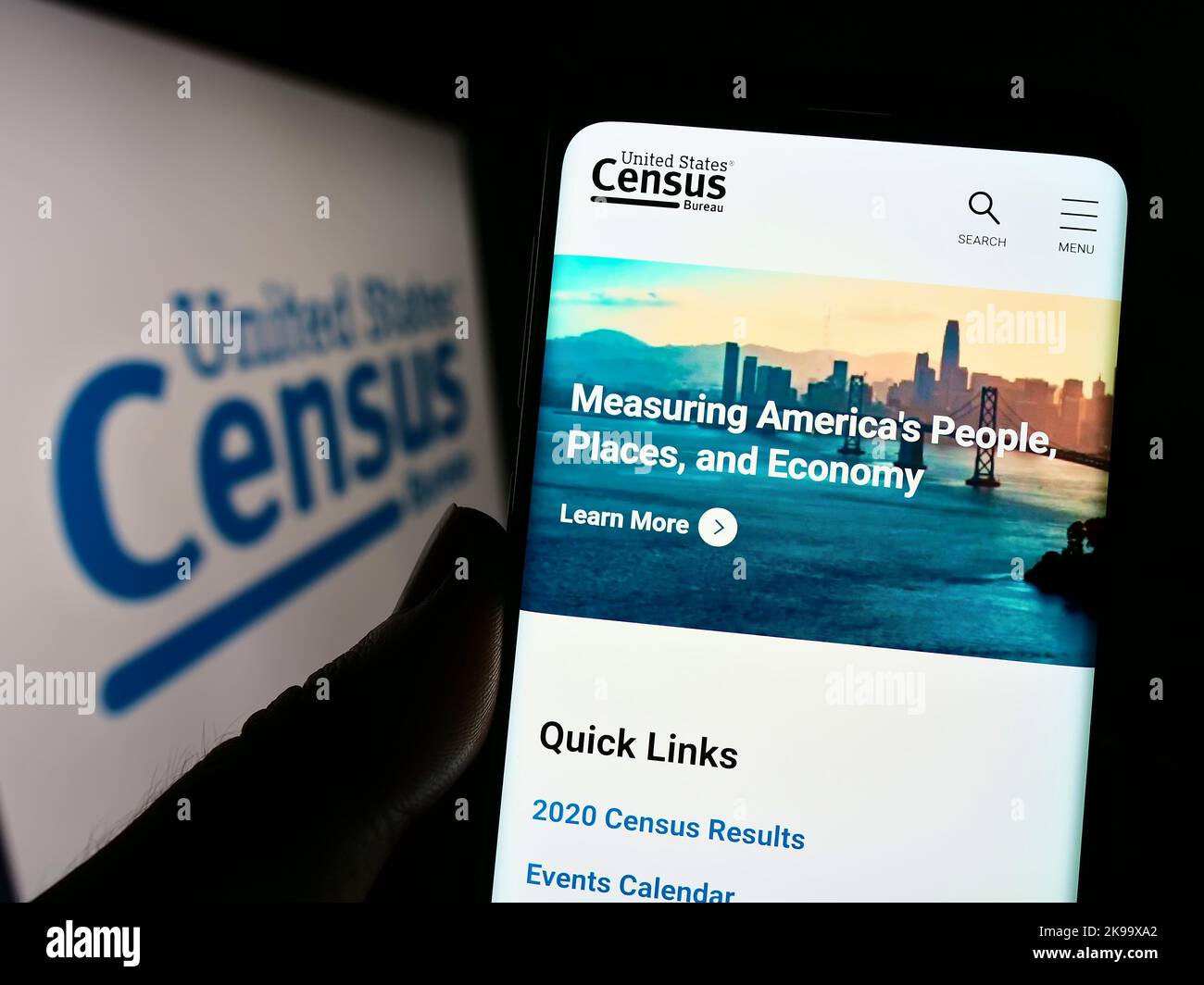 Persona che tiene il cellulare con il sito web dell'United States Census Bureau (USCB) sullo schermo di fronte al logo. Messa a fuoco al centro del display del telefono. Foto Stock