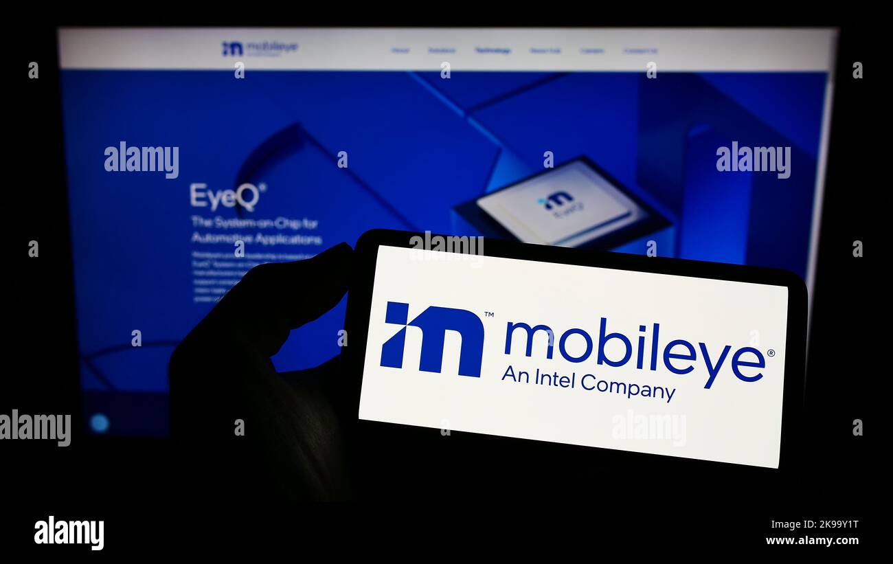 Persona che tiene il cellulare con il logo della società di guida autonoma israeliana Mobileye sullo schermo di fronte al sito web aziendale. Messa a fuoco sul display del telefono. Foto Stock