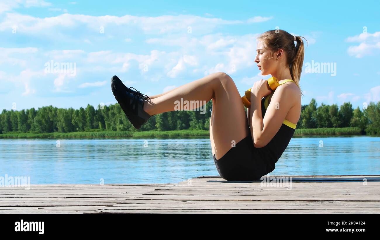 Bella, atletica giovane donna bionda stretching, swings press. Lago, fiume, cielo blu e foresta sullo sfondo, estate giorno di sole. Foto di alta qualità Foto Stock