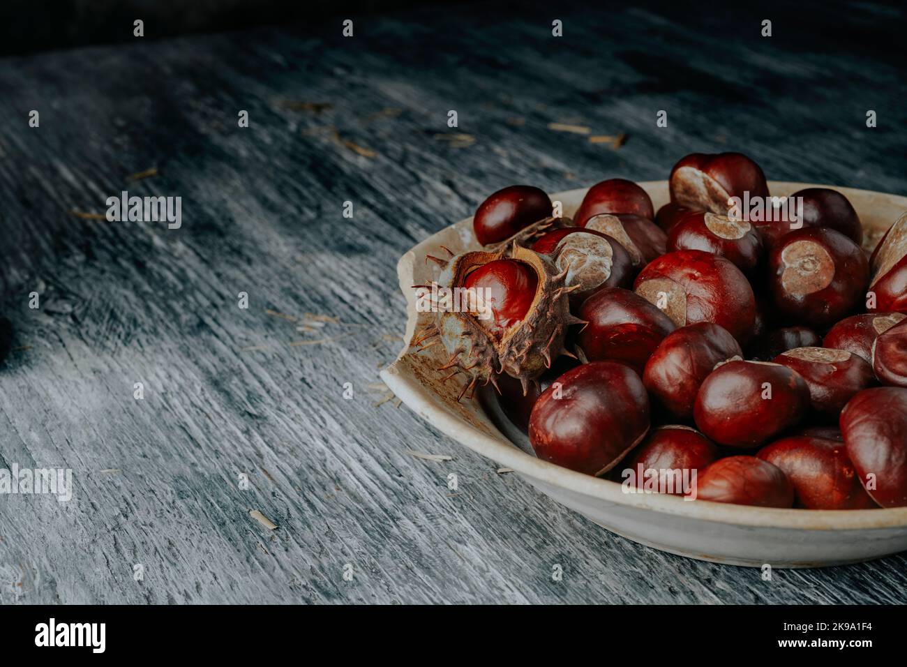 closeup di alcune castagne su un piatto vecchio e stagionato, posto su un rustico tavolo di legno grigio Foto Stock
