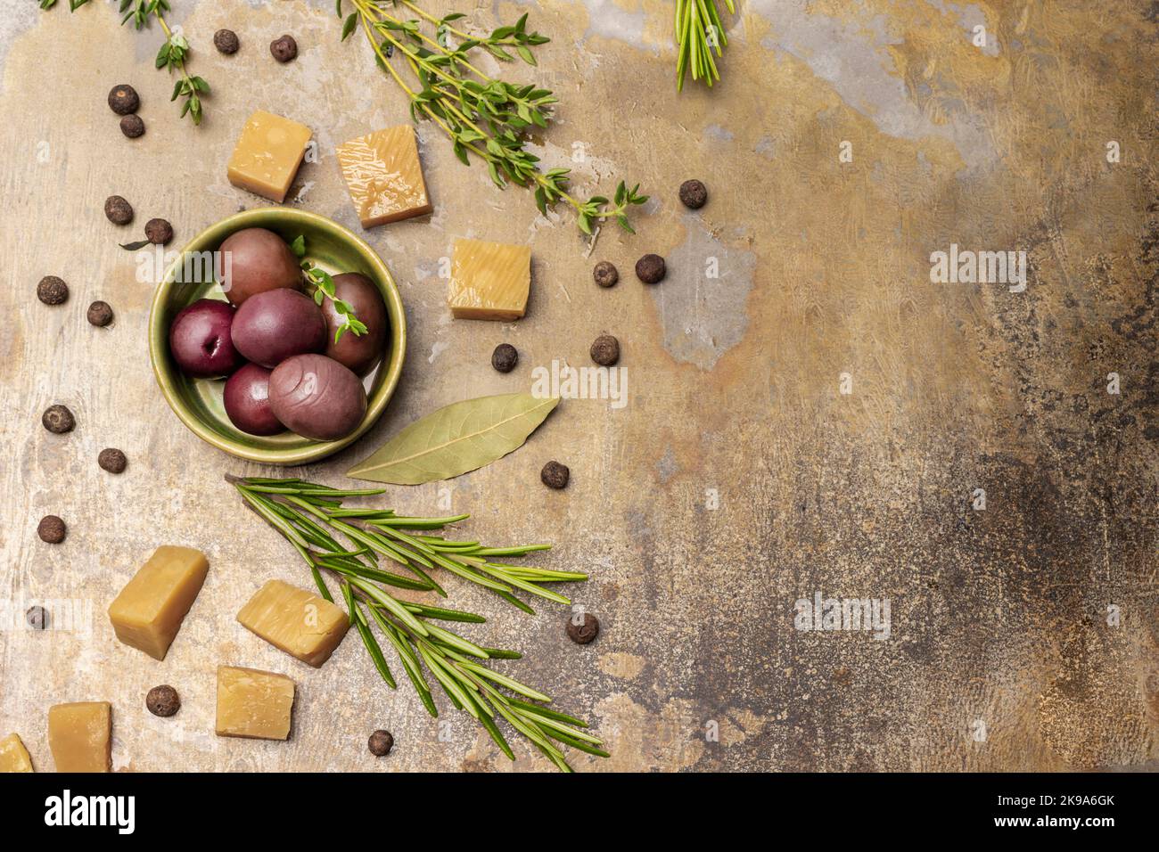 Olive di Borgogna in ciotola, rametto di rosmarino e pezzetti di formaggio. Spazio di copia. Giacitura piatta. Fondo in metallo arrugginito. Foto Stock