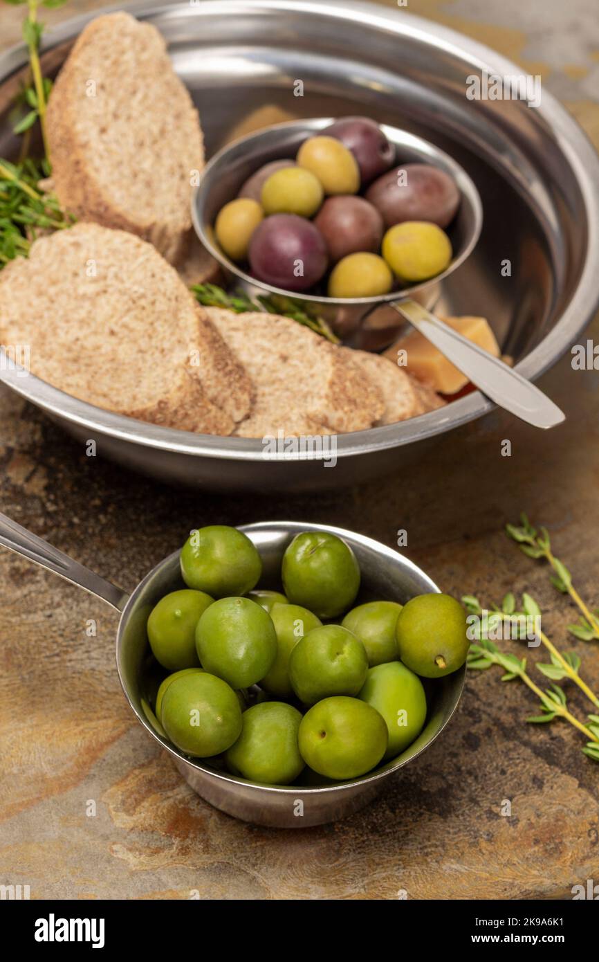 Olive verdi in una ciotola di metallo. Pezzi di baguette e olive in una ciotola. Vista dall'alto. Fondo in metallo arrugginito. Foto Stock