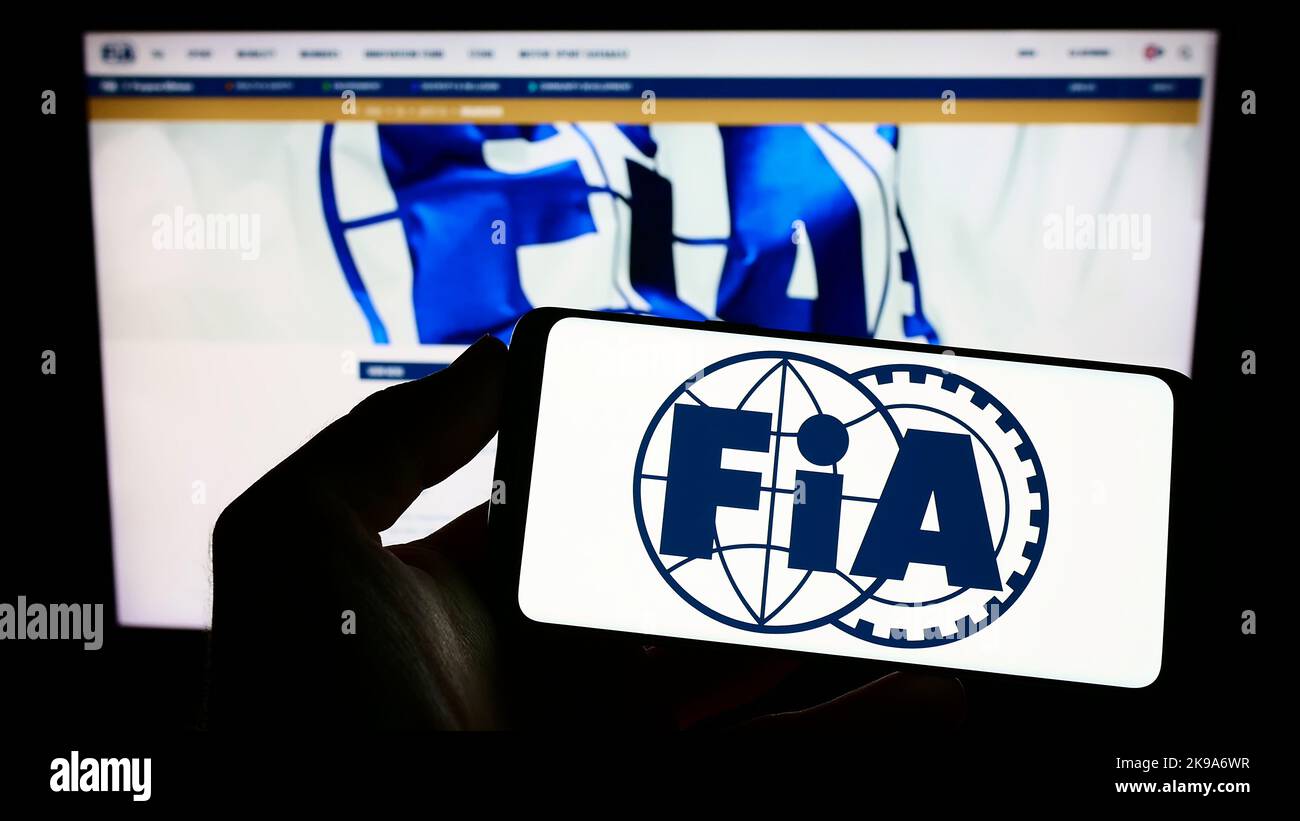 Persona che tiene uno smartphone con il logo della Federazione Internazionale dell'Automobile (FIA) sullo schermo di fronte al sito web. Messa a fuoco sul display del telefono. Foto Stock