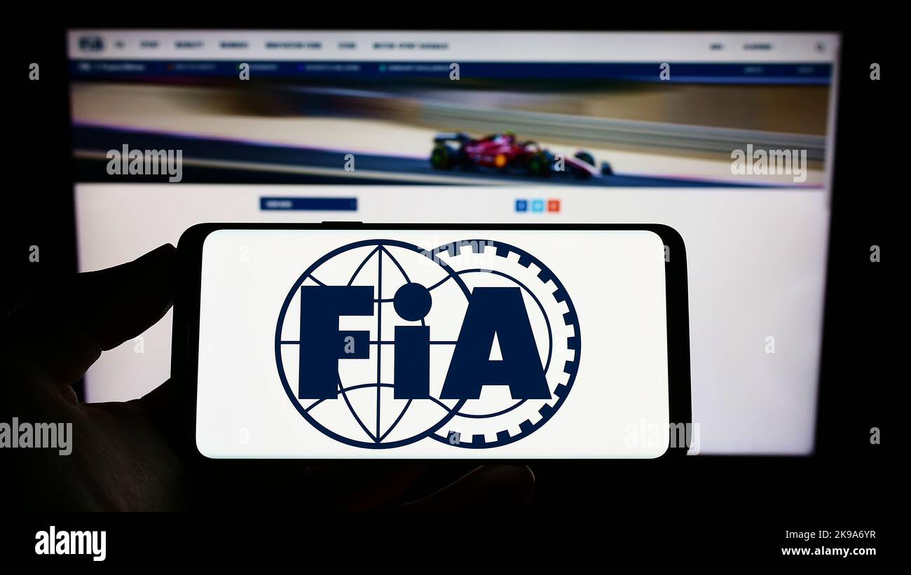 Persona che tiene il cellulare con il logo della Federazione Internazionale dell'Automobile (FIA) sullo schermo di fronte alla pagina web. Messa a fuoco sul display del telefono. Foto Stock
