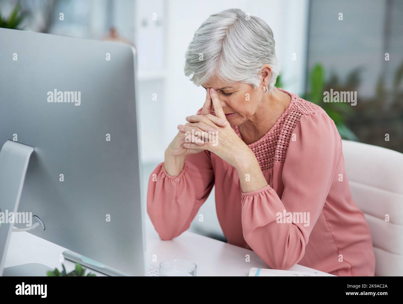 Questa situazione mi sta dando più capelli grigi. Una donna matura che guarda stressato nel suo ufficio al lavoro. Foto Stock