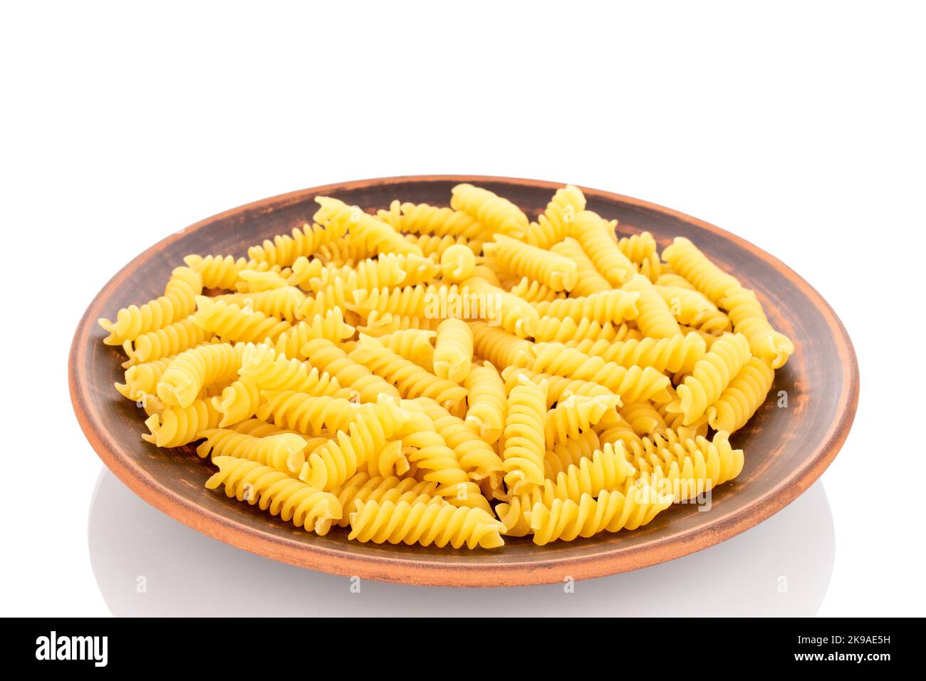 Pasta di grano duro su piatto di argilla, macro, isolata su fondo bianco. Foto Stock