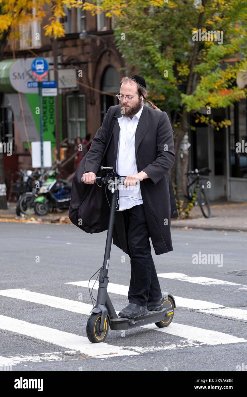 Un uomo ebraico ortodosso attraversa Lee Avenue sul suo scooter elettrico. A Brooklyn, New York, autunno 2022. Foto Stock