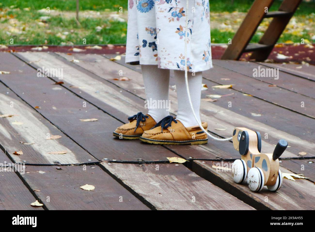 le gambe di una bambina e di una sedia a rotelle giocattolo di legno. belle scarpe per bambini. colori dell'autunno Foto Stock