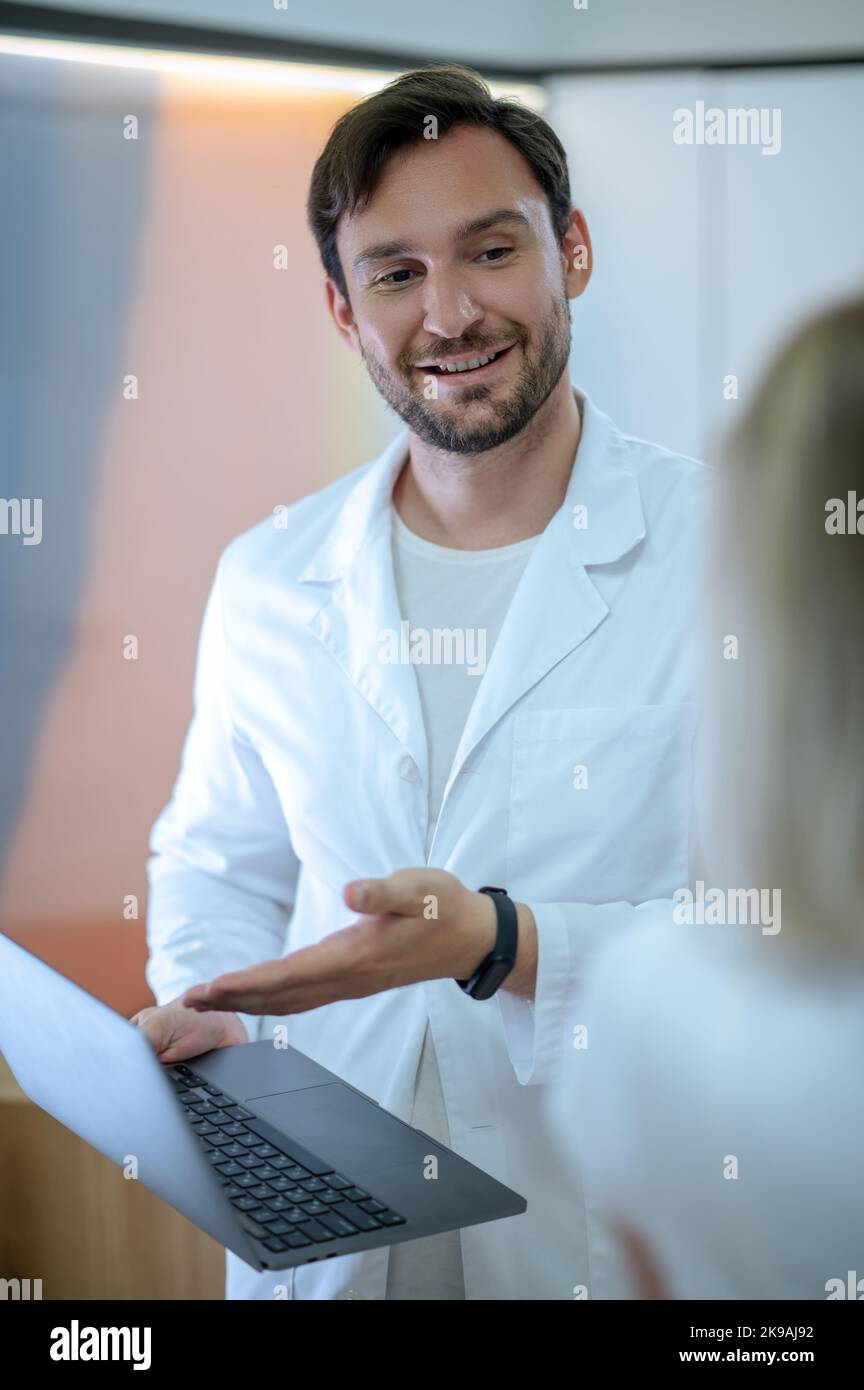 Medico allegro che riceve una donna malata nel suo ufficio Foto Stock