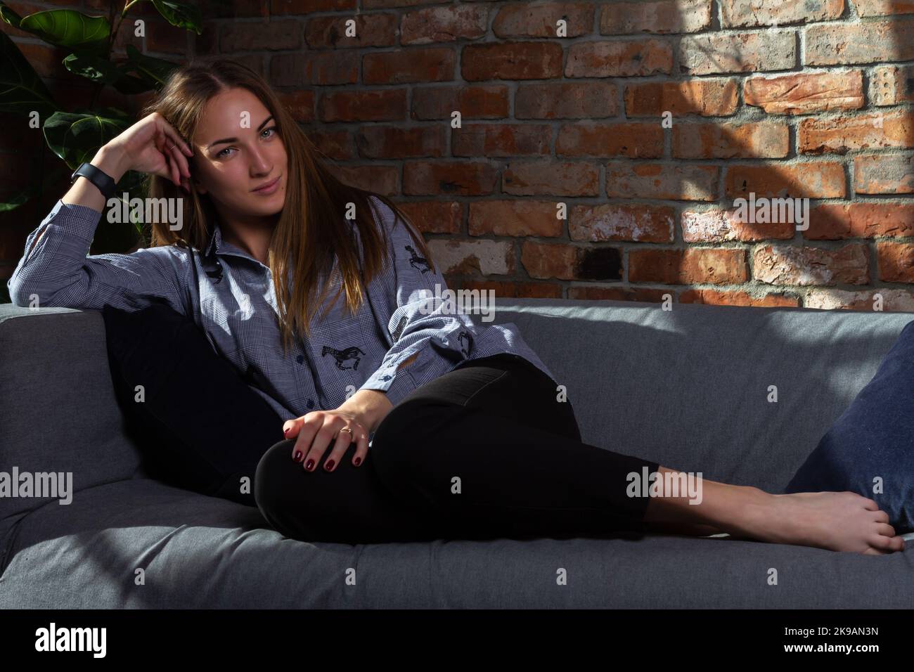 Donna in una camicia blu che si rilassa sul divano, guardando nella macchina fotografica Foto Stock