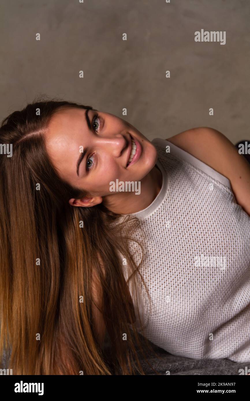 Donna sorridente dai capelli lunghi in una parte superiore bianca che guarda nella macchina fotografica Foto Stock