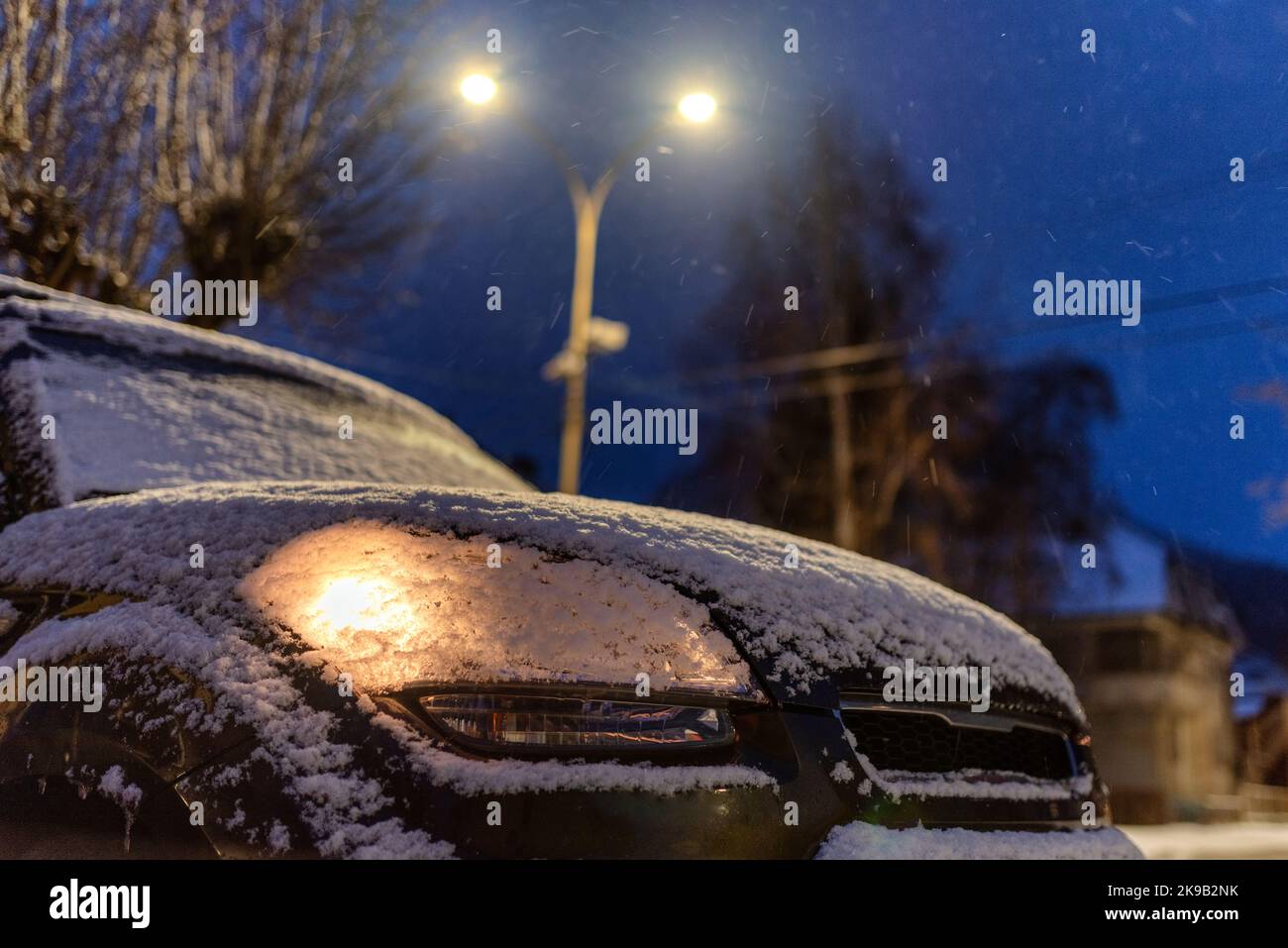 Auto parcheggiata con luce coperta di neve di notte. Foto Stock