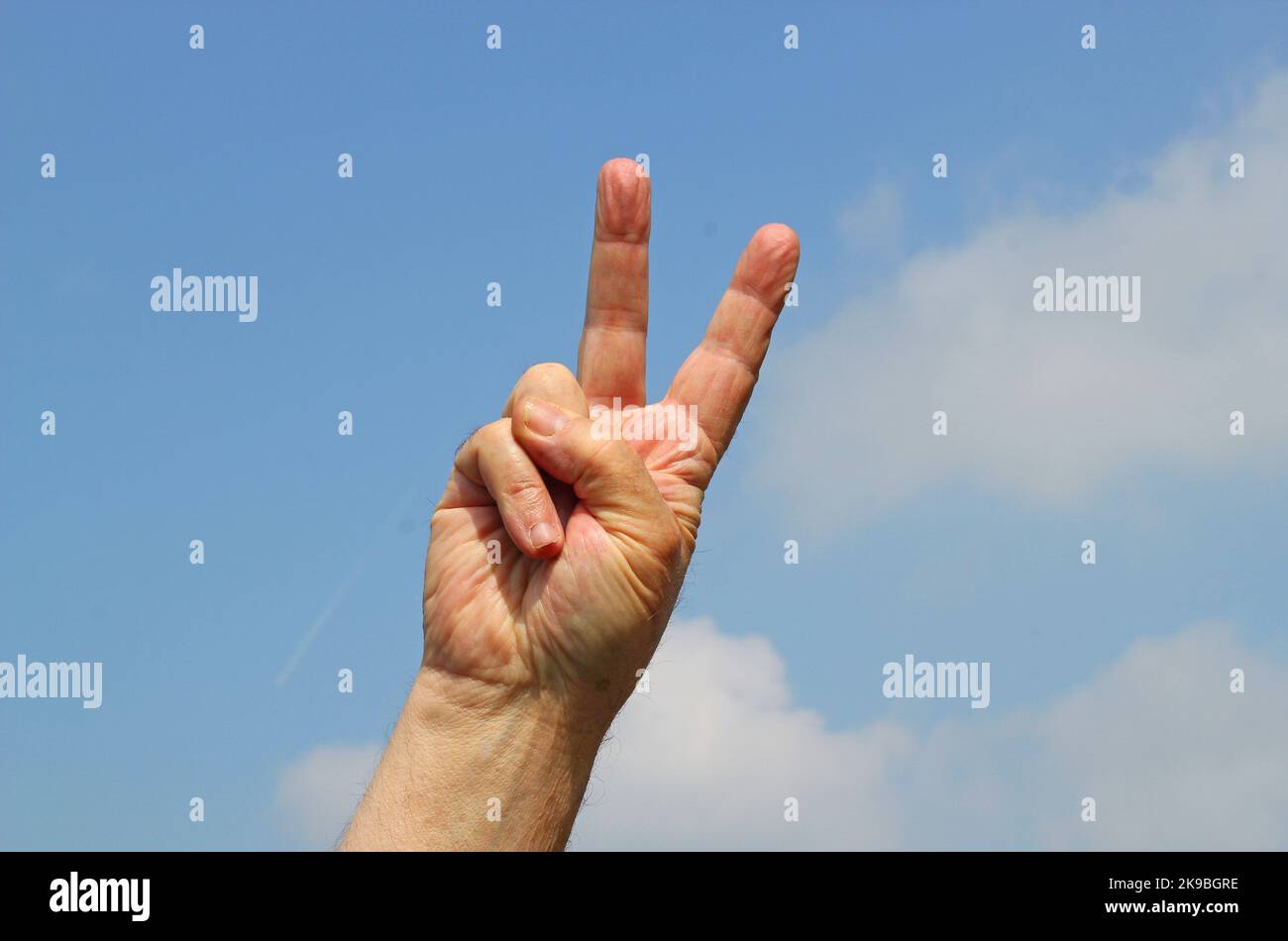 Due dita segno di pace. Mano su con sfondo cielo blu. Un segnale che chiede pace e anche un saluto. Foto Stock